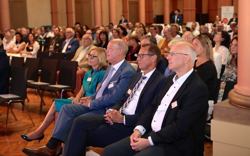 Ausschnitt aus einer Vernastaltung mit verschiedenen Personen im Plenum